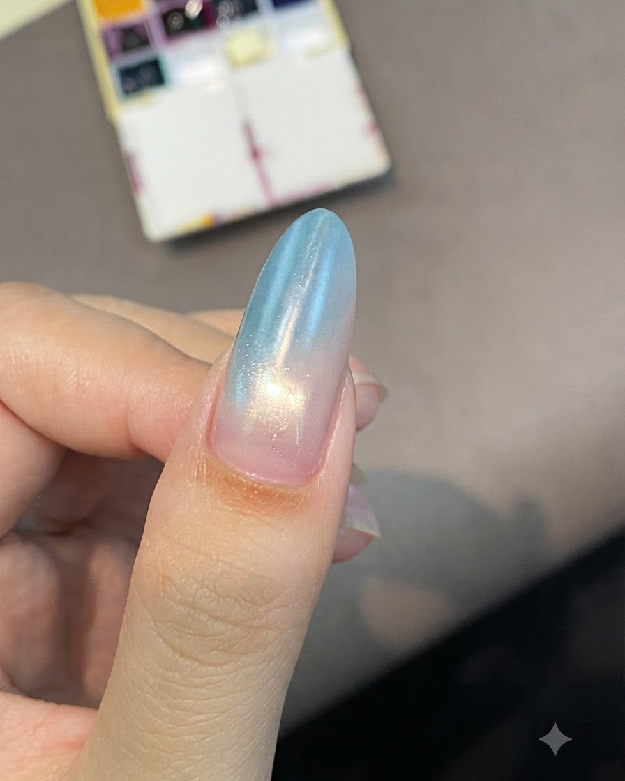 Ein mandelförmiger Nagel mit einem sanften Blau-zu-Rosa-Verlauf zeigt Glanz beim Aushärten unter Licht.