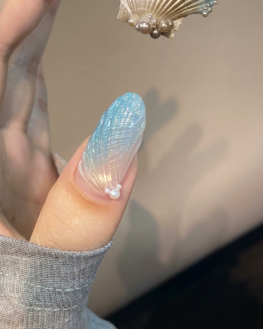 Ein Fingernagel mit blauer und transluzenter Muschel-Nail-Art liegt unter einer violetten UV-Lampe zum Aushärten.