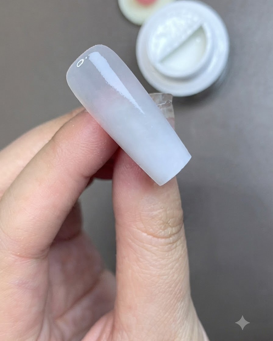 Ein Pinsel trägt eine glatte Schicht matten Top Coat auf einen vorbereiteten, milchig-weißen Nagel auf.