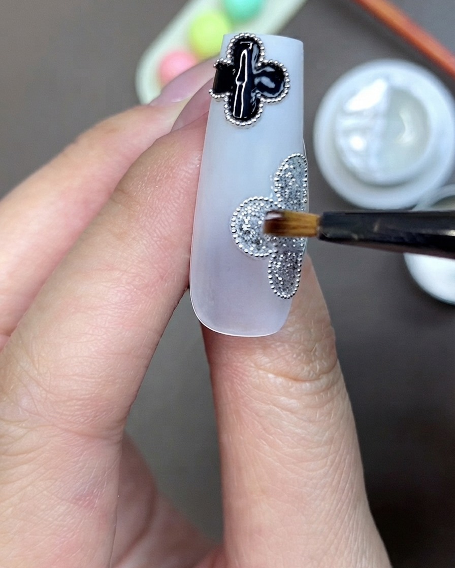 Ein Pinsel trägt klares Strassstein-Klebegel in der Mitte eines silbernen Glitzer-Kleeblattmotivs auf einem Nagel auf.