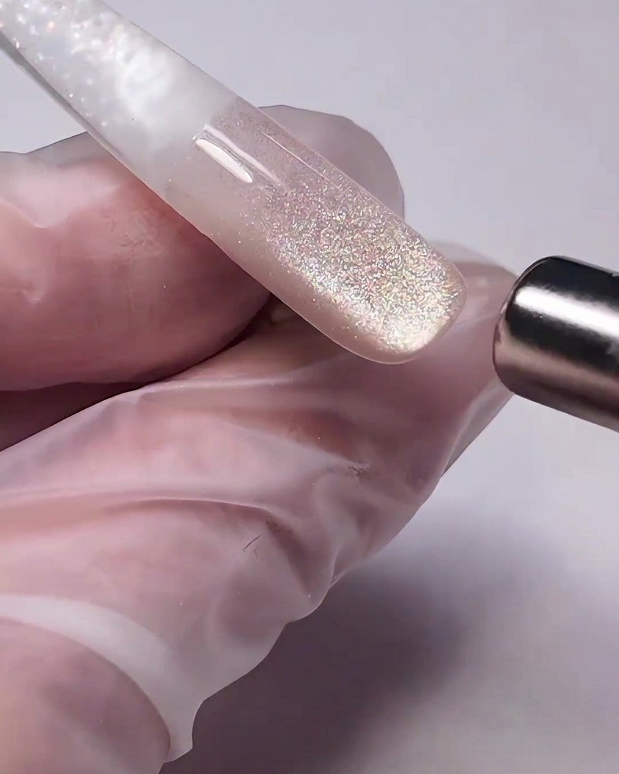 Ein zylindrischer Magnetstab wird nah an das feuchte Cat-Eye-Gel auf einem Nagel gehalten und zieht die Metallpartikel zu einem Schimmer zusammen.