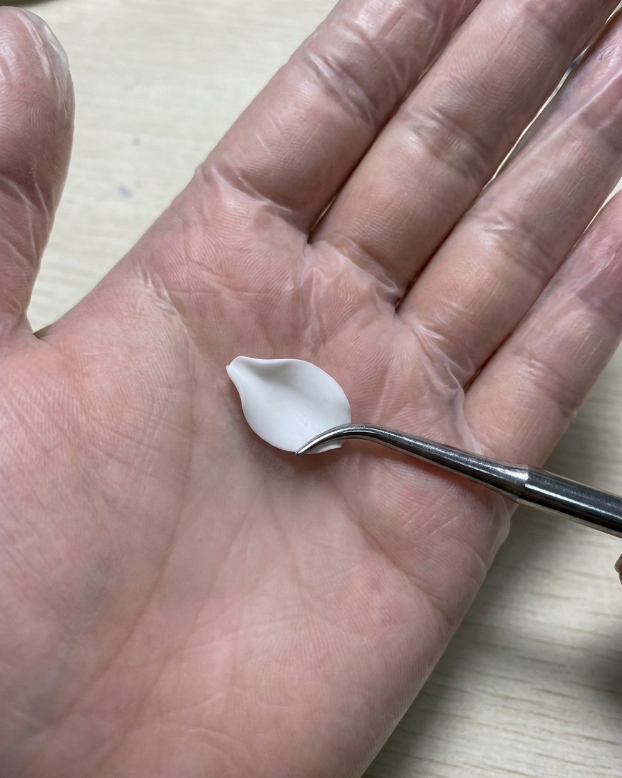 Eine behandschuhte Hand hält ein Silikon-Modellierwerkzeug und glättet ein weißes 3D-Gel-Blütenblatt, das auf einer Silikonmatte liegt.
