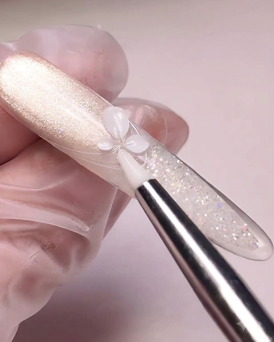 Ein Silikonwerkzeug drückt weißes Modelliergel zu Blumenblättern auf einer mit Cat-Eye lackierten Nagelspitze.