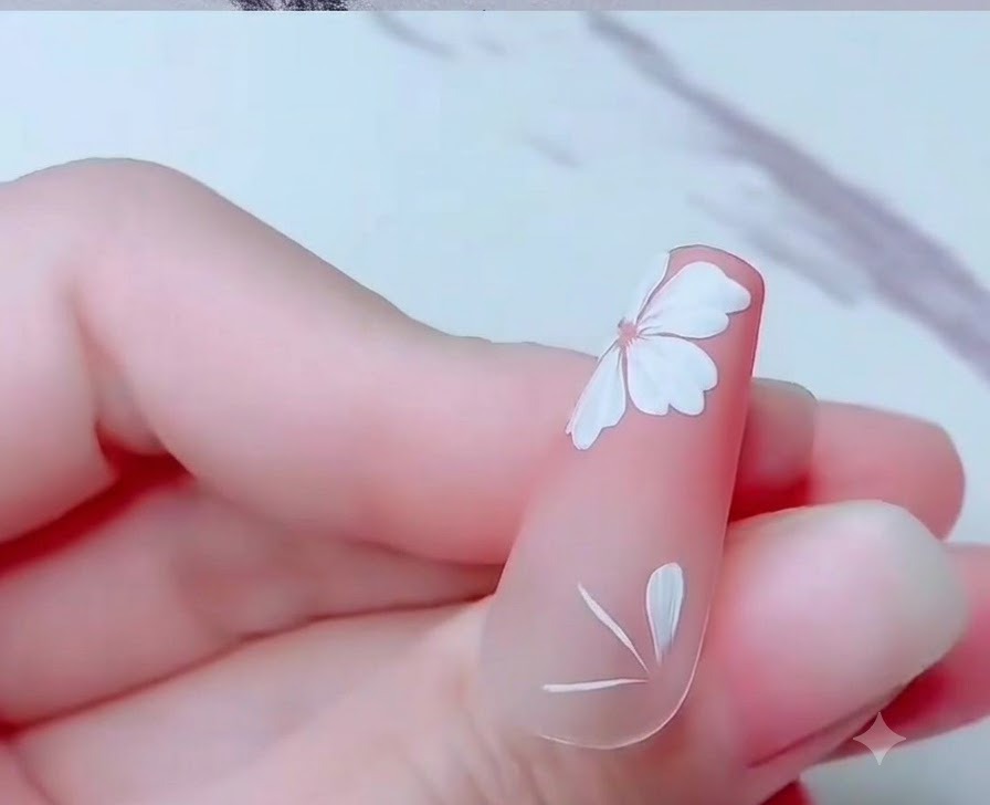 Nahaufnahme eines Nagels mit teilweise gemalten weißen Kirschblütenblättern nahe der Unterkante.