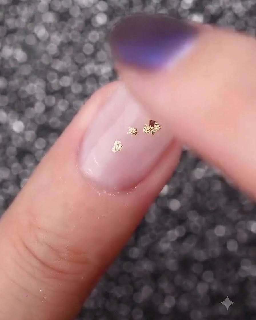 Ein Finger drückt Blattgoldflocken sanft nach unten, um sie flach an der gewölbten Nageloberfläche zu befestigen.