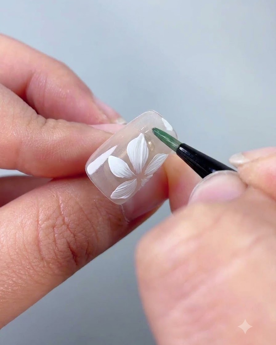 Ein Liner-Pinsel trägt grünes Gel auf, um ein dünnes Blatt neben der weißen Blüte zu formen.