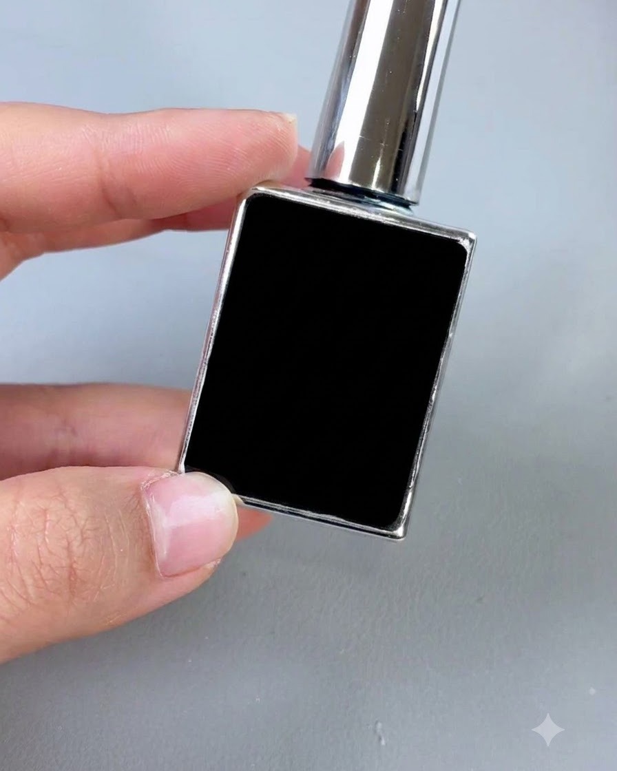 Eine kleine schwarze Kosmetikflasche mit silberner Kappe und Applikatorpinsel auf grauem Hintergrund.