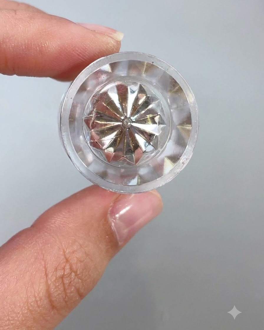 Eine Nahaufnahme einer klaren, facettierten Kristallbehälterkappe oder eines Applikators, die Licht vor hellen Hintergrund reflektiert.
