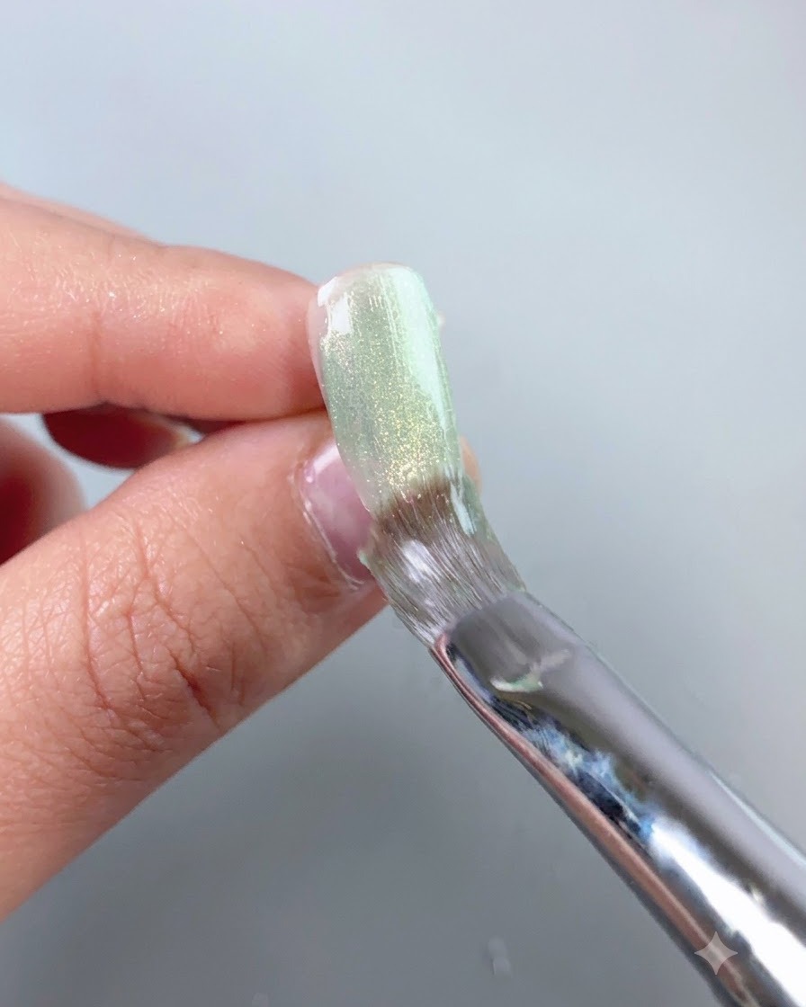 Ein Nagelpinsel glättet eine schier grüne Cat-Eye-Gelschicht über eine Press-on-Nageloberfläche.