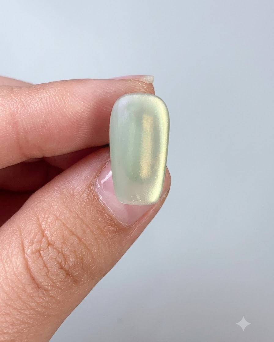Ein Nagelpinsel trägt Top-Coat über einen grünen Cat-Eye-Gel-Nagel auf.