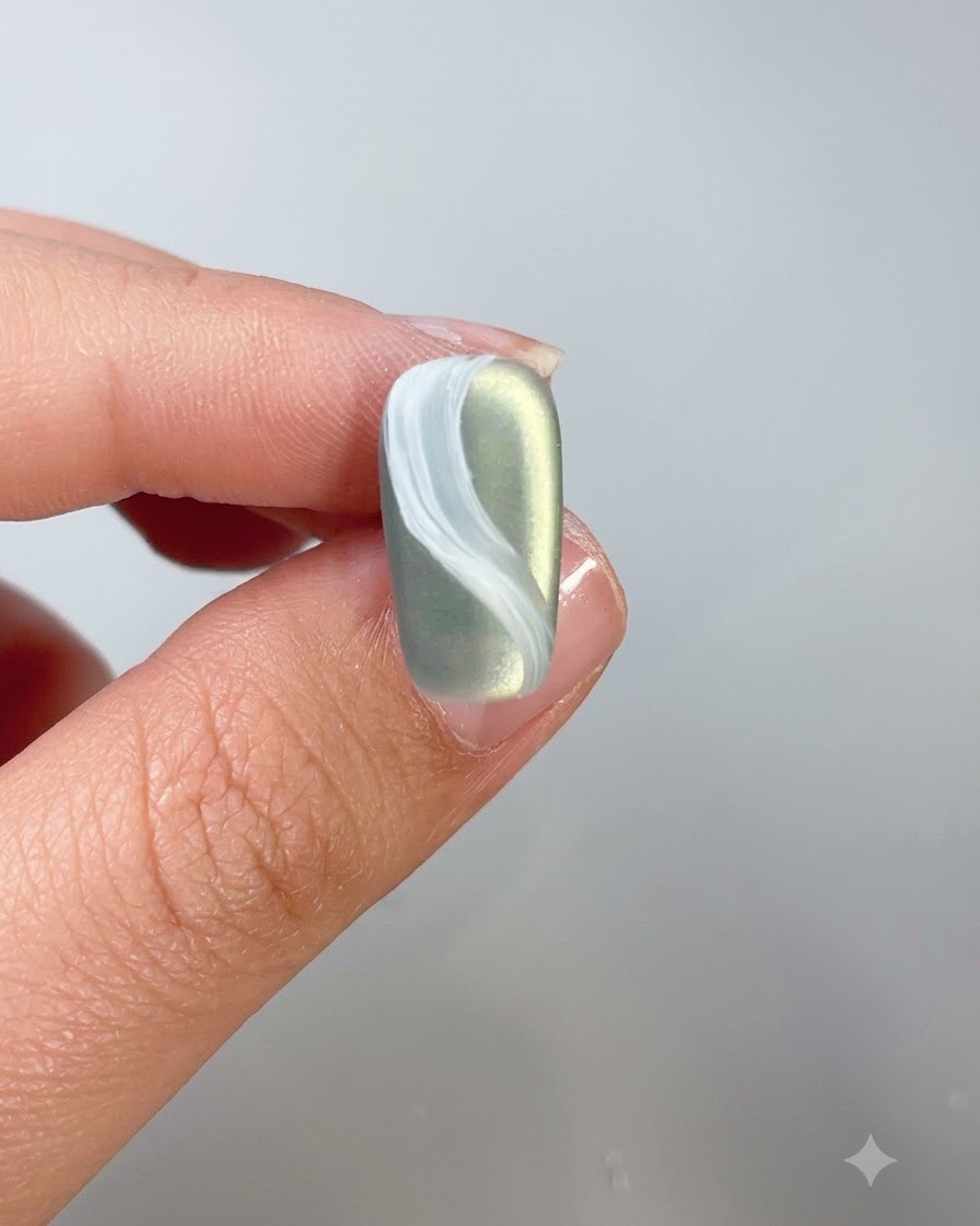Nahaufnahme eines Nagels mit weißem Wolkendesign, der mit Top-Coat überzogen wird.