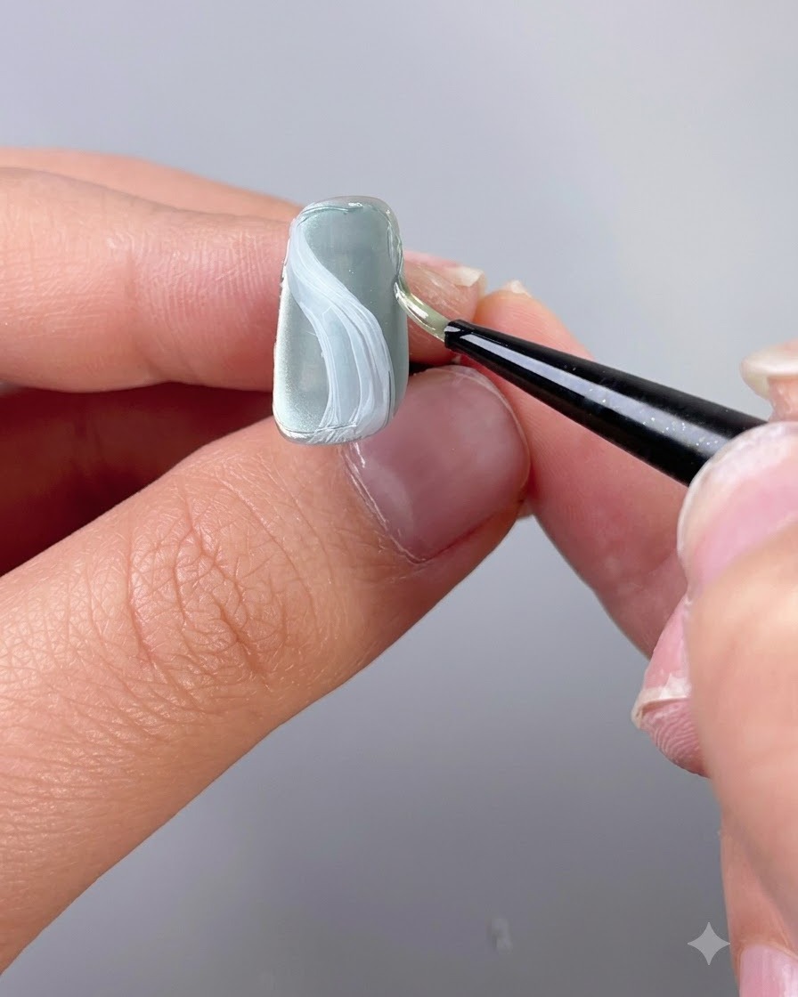 Ein feiner Detailpinsel trägt Textur-Modelliergel entlang der Kante eines Nagels auf.