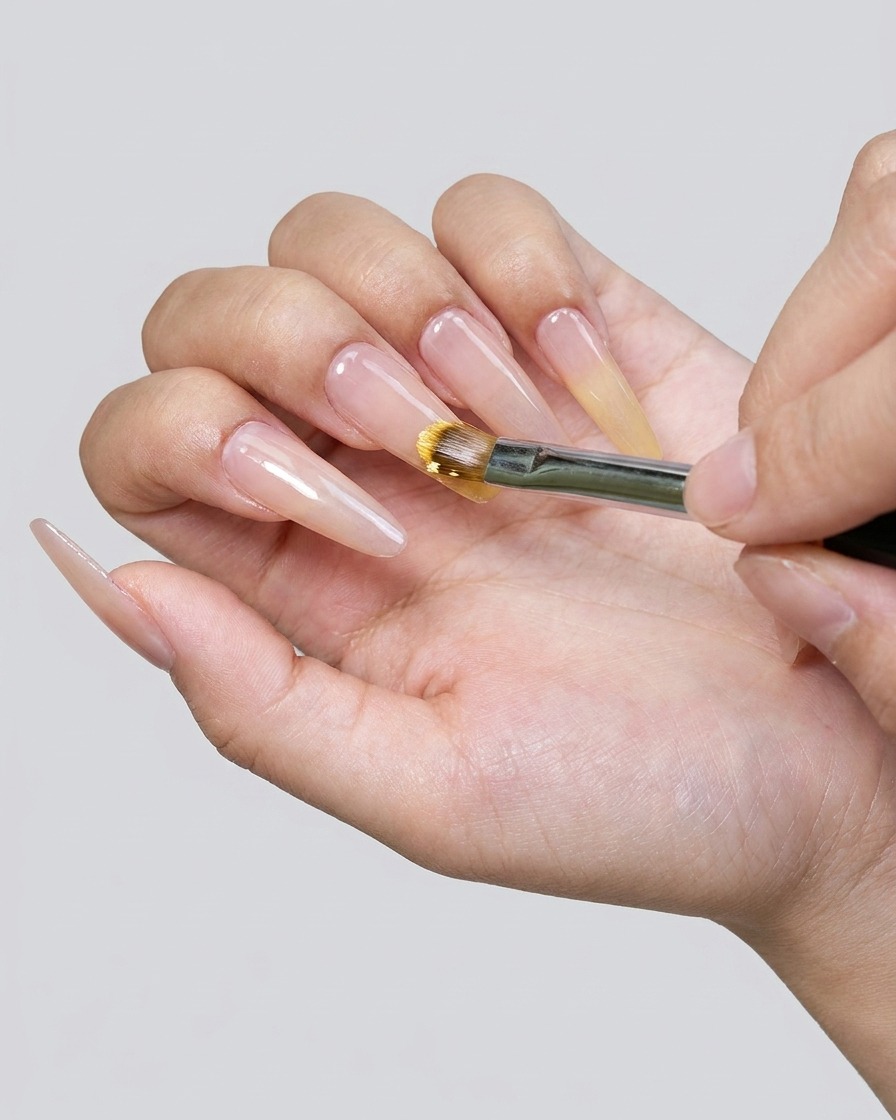 Nahaufnahme eines Pinsels beim Auftragen von gelbem Gel-Nagellack auf die Nagelspitze.