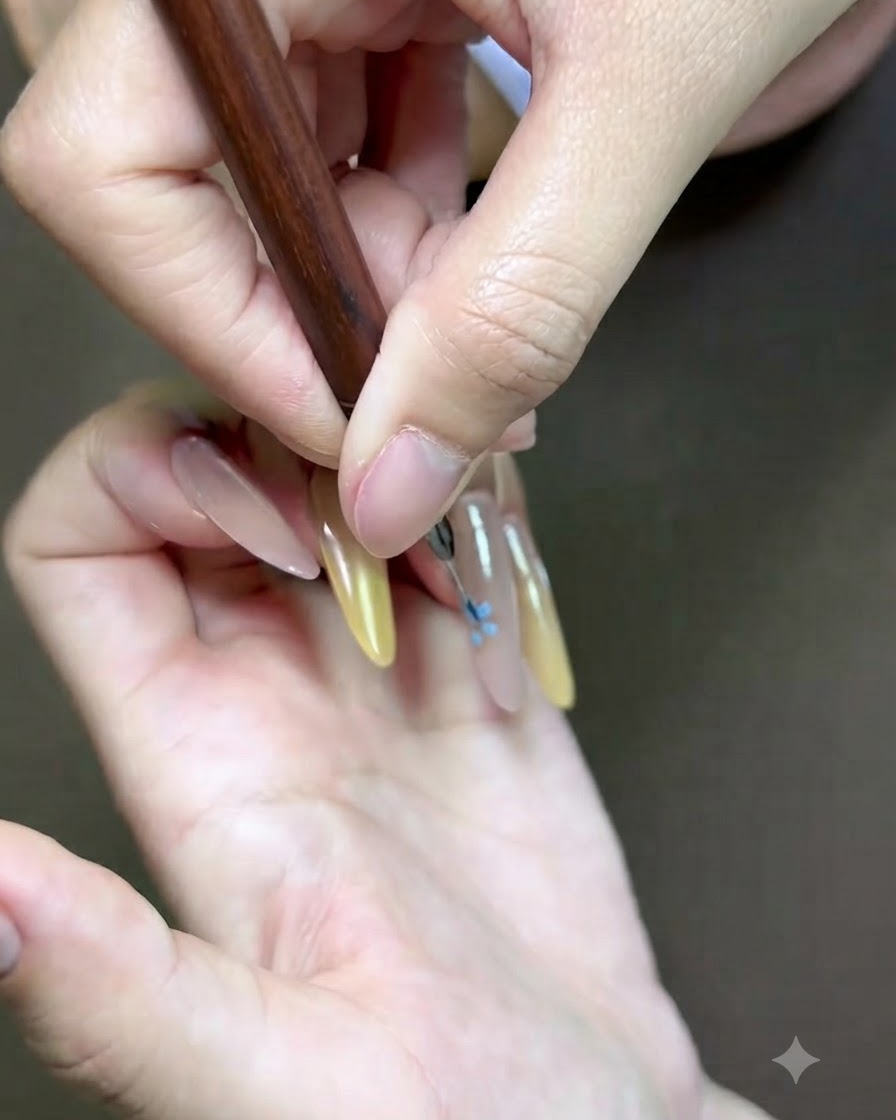 Eine detaillierte Nahaufnahme eines feinen Nail-Art-Pinsels, der einen pinkfarbenen Blumenakzent auf den Nagel malt.