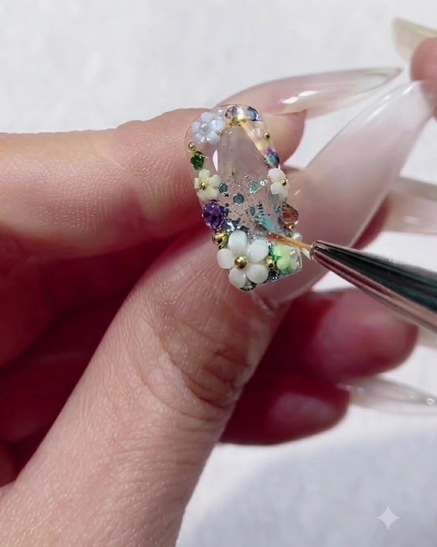 Ein Liner-Pinsel füllt die winzigen Zwischenräume zwischen bunten Strasssteinen und Perlen auf einem Nagel mit Gel.