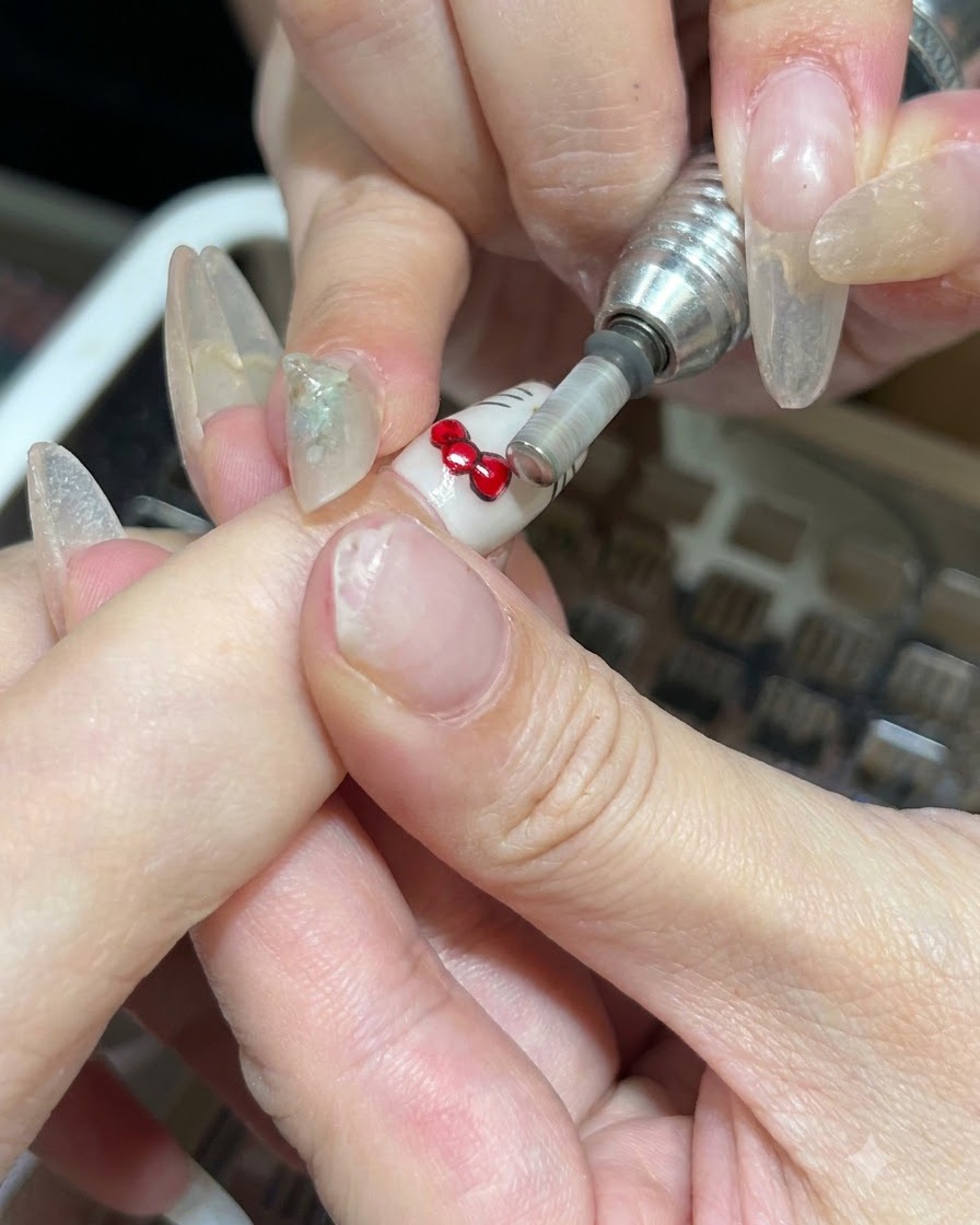 Eine elektrische Nagelfeile mit Metallbit entfernt altes Nageldesign von einem Fingernagel.