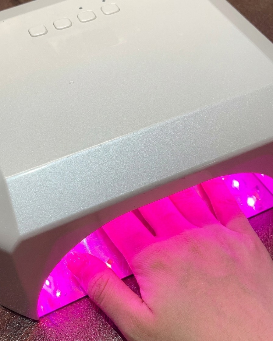 Eine Hand in einer großen Standard UV/LED Nagellampe strahlt während des Aushärtens rosa Licht aus.