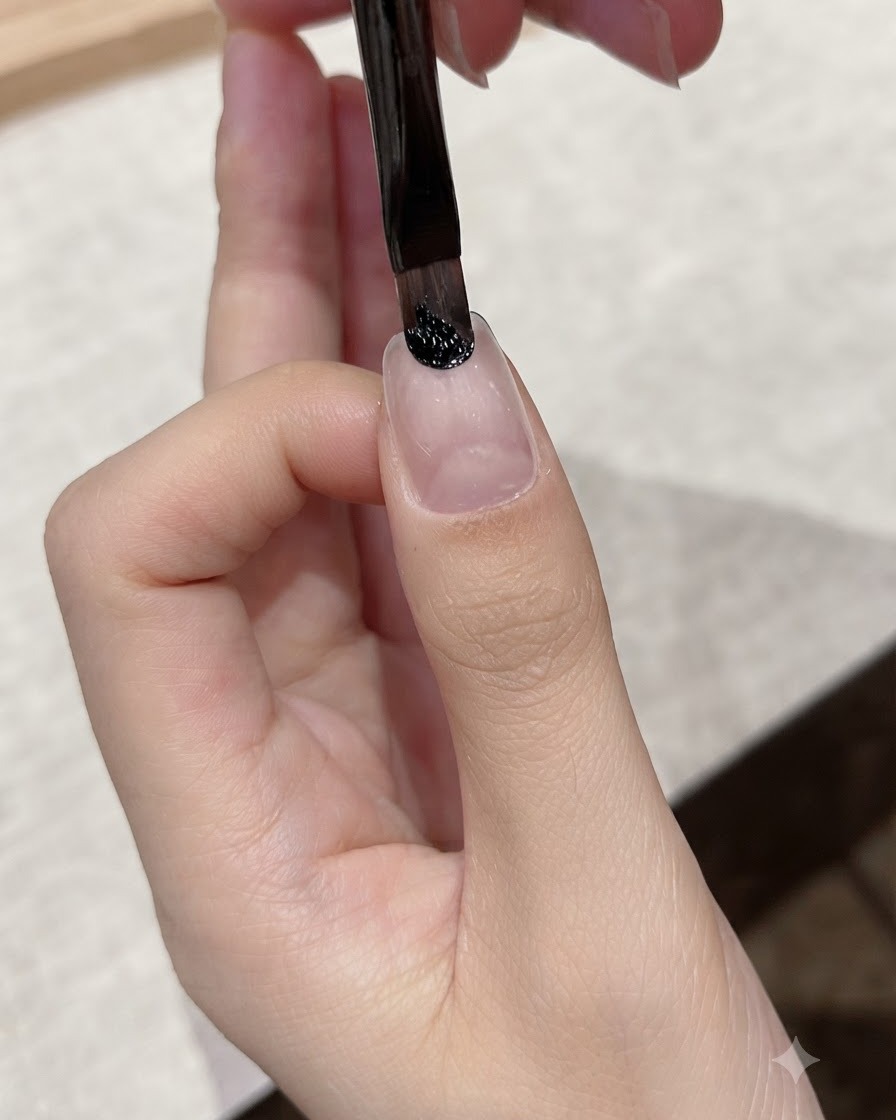 Ein feiner Linerpinsel trägt dunkles schwarzes Gel im Nagelhautbereich eines Naturnagels auf.