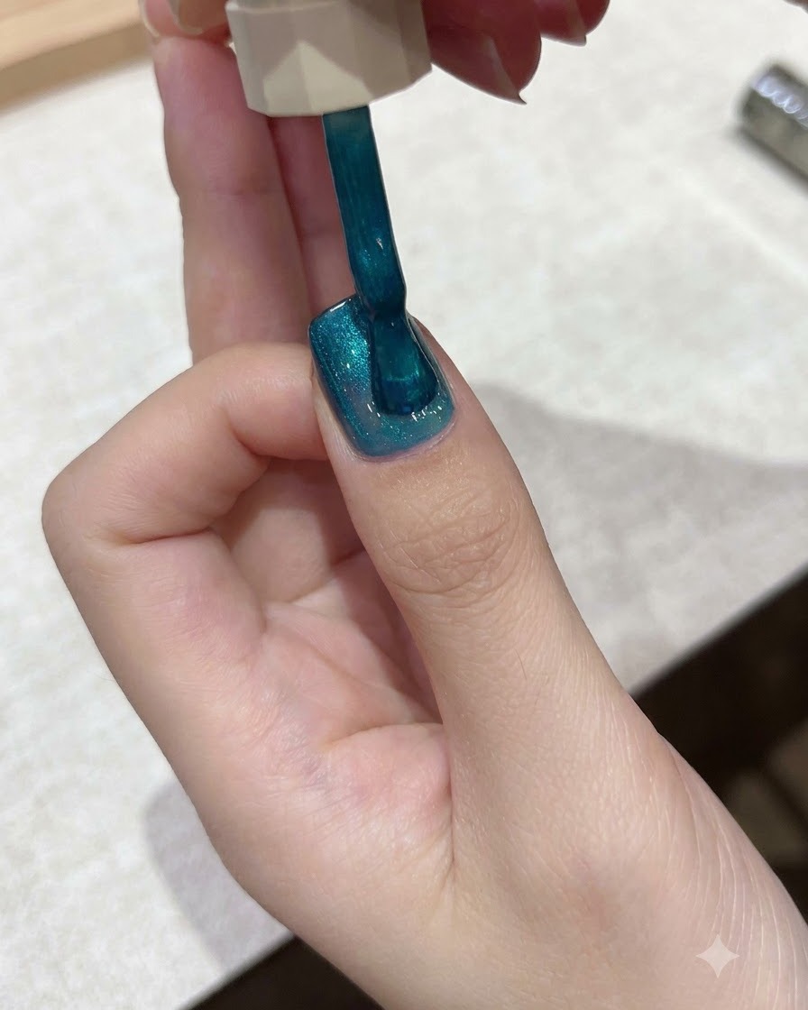 Ein Pinsel trägt lebendigen Teal-blauen Cat-Eye-Gelack gleichmäßig auf die Nageloberfläche auf.