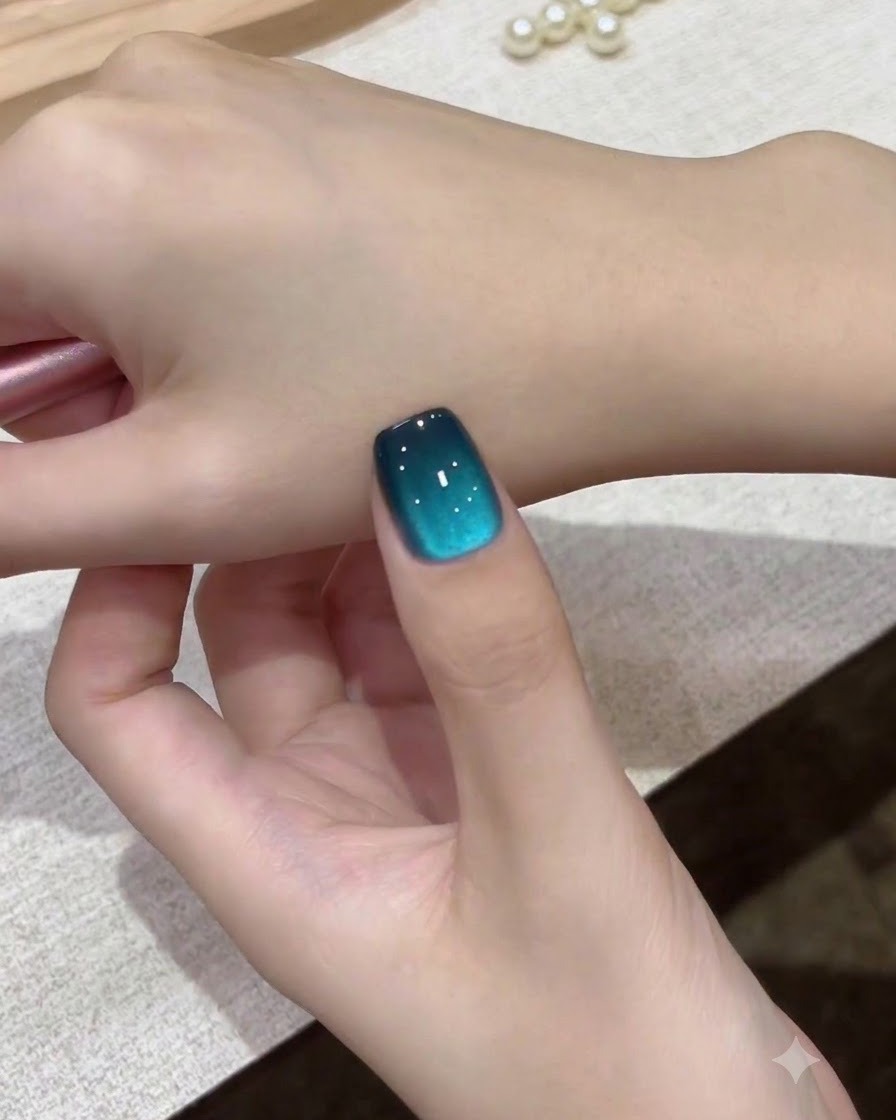 Eine Nahaufnahme eines einzelnen Teal-Galaxy-Cat-Eye-Nagels vor dem Handrücken gehalten.