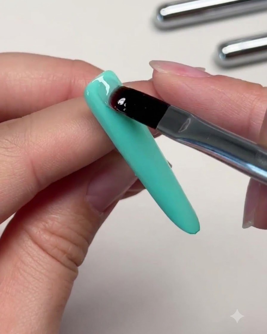 Ein Pinsel, der einen klaren Tropfen Verstärkungsgel auf den oberen Bereich eines mintgrünen Nagels platziert, um einen Apex aufzubauen.