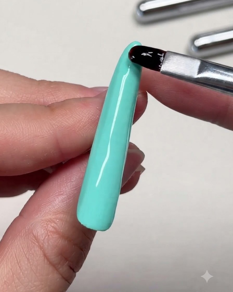 Eine Nahaufnahme einer Bürste, die Verstärkungsgel in der Nähe der Spitze einer langen Nagelverlängerung nivelliert.