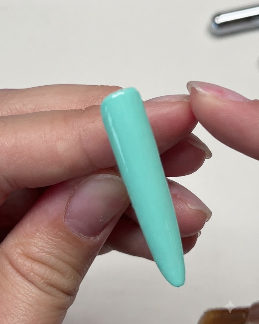 Ein Pinsel, der einen matten Topcoat über die solide mintgrüne Nagelverlängerung aufträgt.
