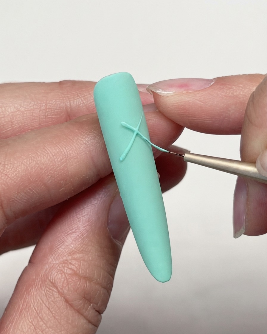 Eine Nahaufnahme eines feinen Liner-Pinsels, der Gelliniers auf einer mintgrünen matten Nagelspitze kreuzt, um ein Sterndesign zu beginnen.