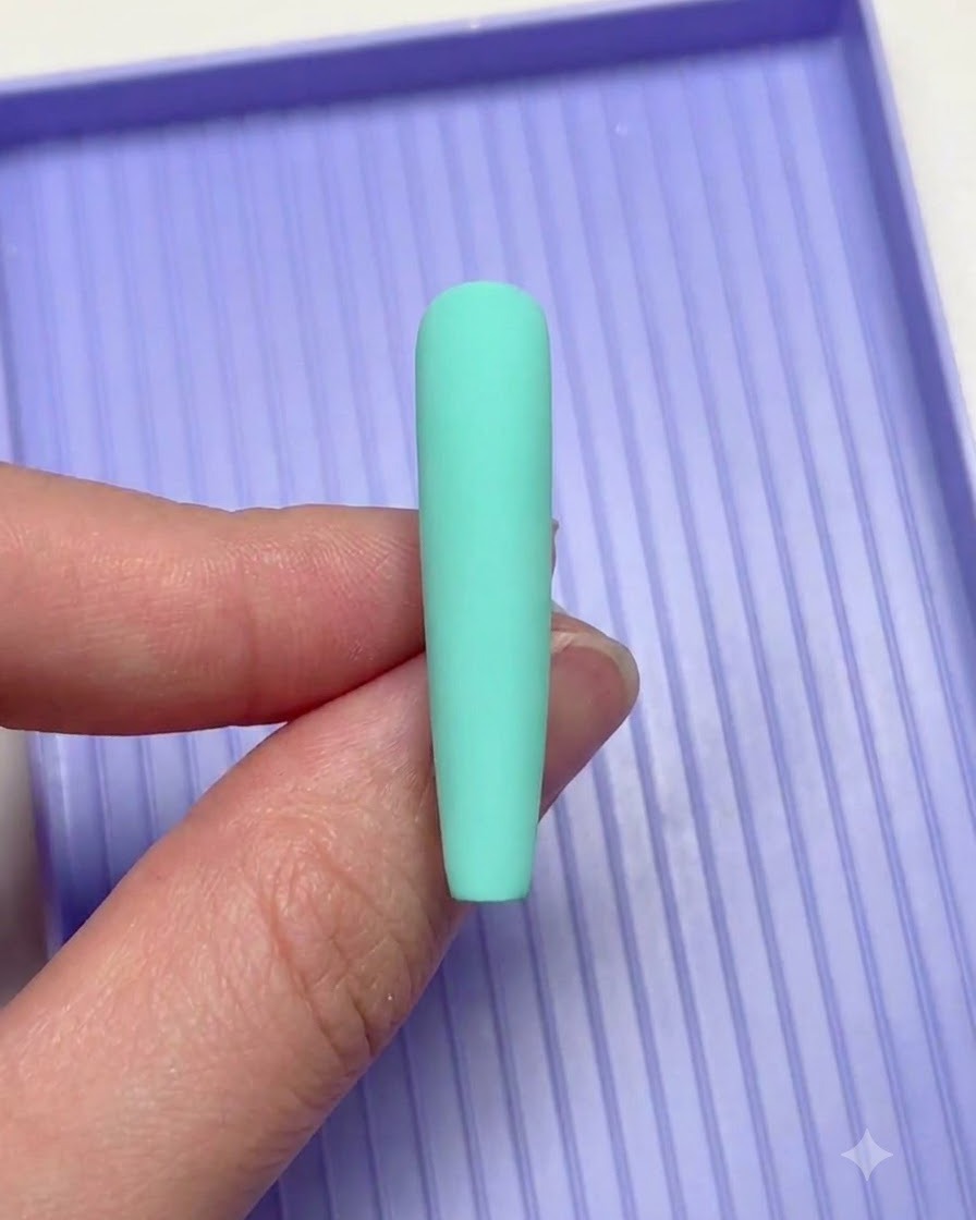 Eine Hand, die einen mintgrünen Nagel während des Nailarts über eine lila Sortierschale hält.