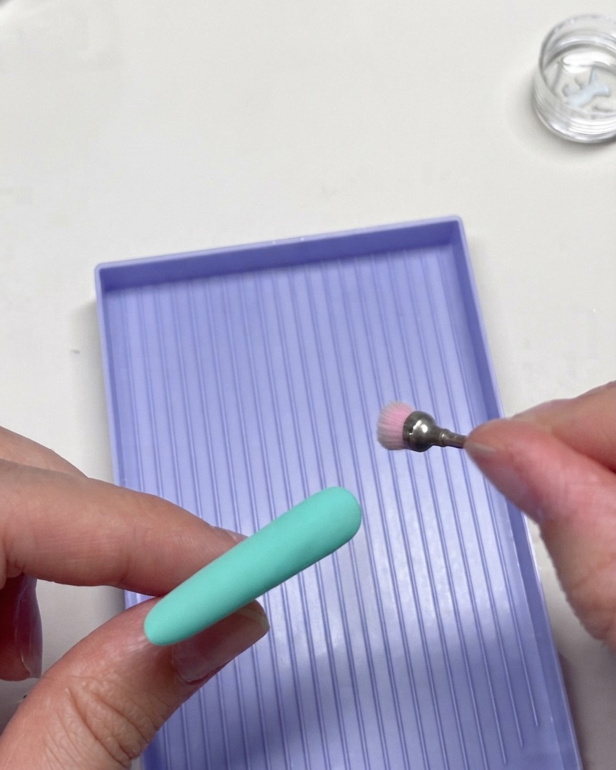 Ein rotierendes Fräser-Werkzeug, das die Kanten einer mintgrünen Nagelspitze sanft verfeinert.