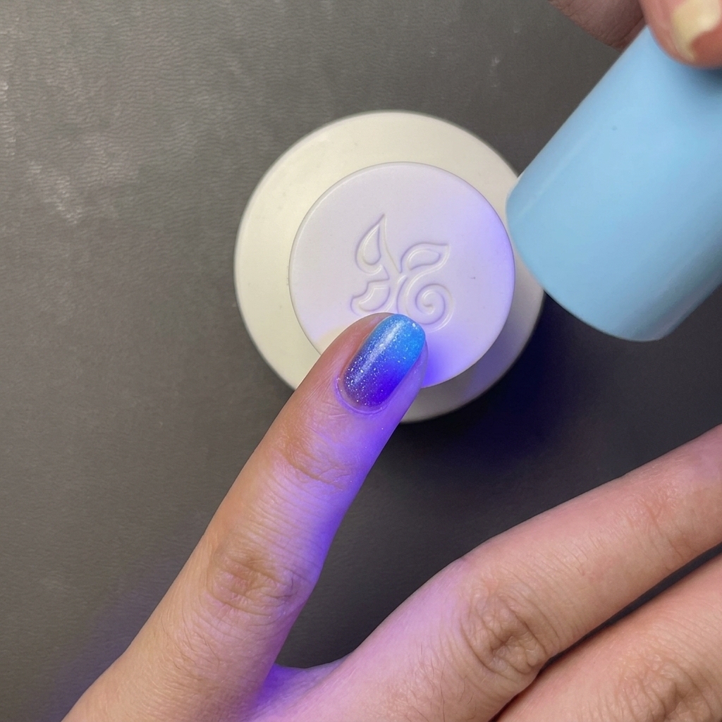 Ein Finger mit hellblauem Gel-Lack wird unter einer tragbaren, hellblauen UV-/LED-Lampe ausgehärtet.