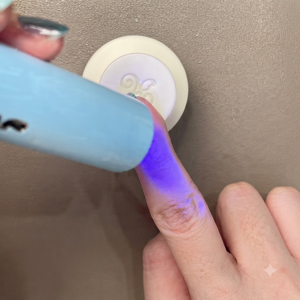 Aushärten eines blau-grünen Cat-Eye-Nagels unter einer kleinen tragbaren blauen UV-/LED-Lampe.