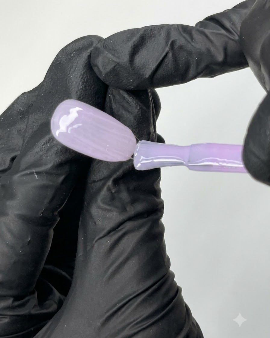 Ein flacher Pinsel gleitet gleichmäßig mit N04 transparentem lila Gel-Nagellack über die Oberfläche einer ovalen Nagelspitze.