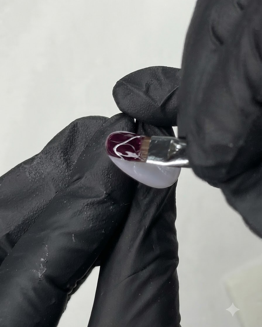 Ein feiner Liner-Pinsel zeichnet zarte weiße geschwungene Linien auf die Oberfläche eines dekorierten Nagels.