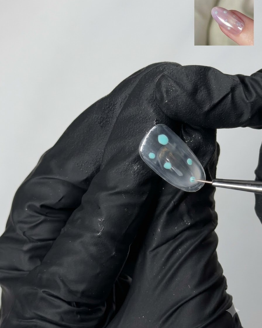 Ein feiner Detailpinsel platziert kleine türkisfarbene Punktakzente auf einer klaren Gel-Nageloberfläche.