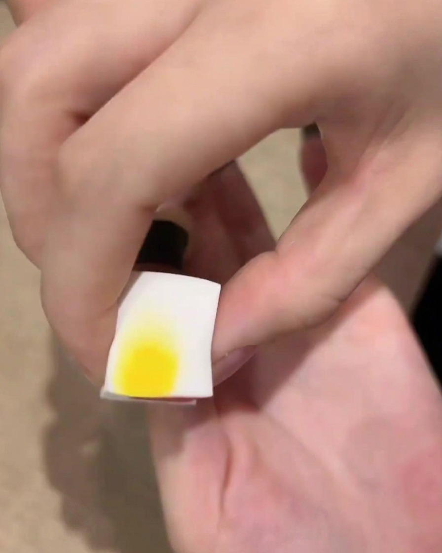Ein weißes Kosmetikschwämmchen mit schwarzem Gellack nah an einem Fingernagel, bereit für den Ombré-Effekt.