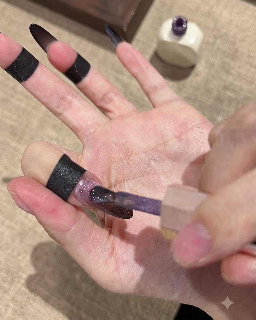 Ein Pinsel trägt das Fallen Gold Cat-Eye-Gel auf einer dunklen Ombré-Nagelbasis auf.