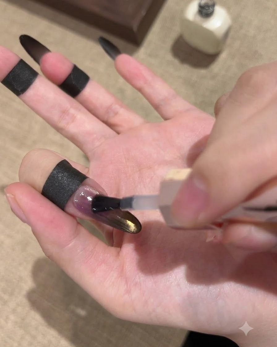 Ein Pinsel trägt einen glänzenden Top Coat über einen schwarz-goldenen Ombré-Cat-Eye-Nagel auf.