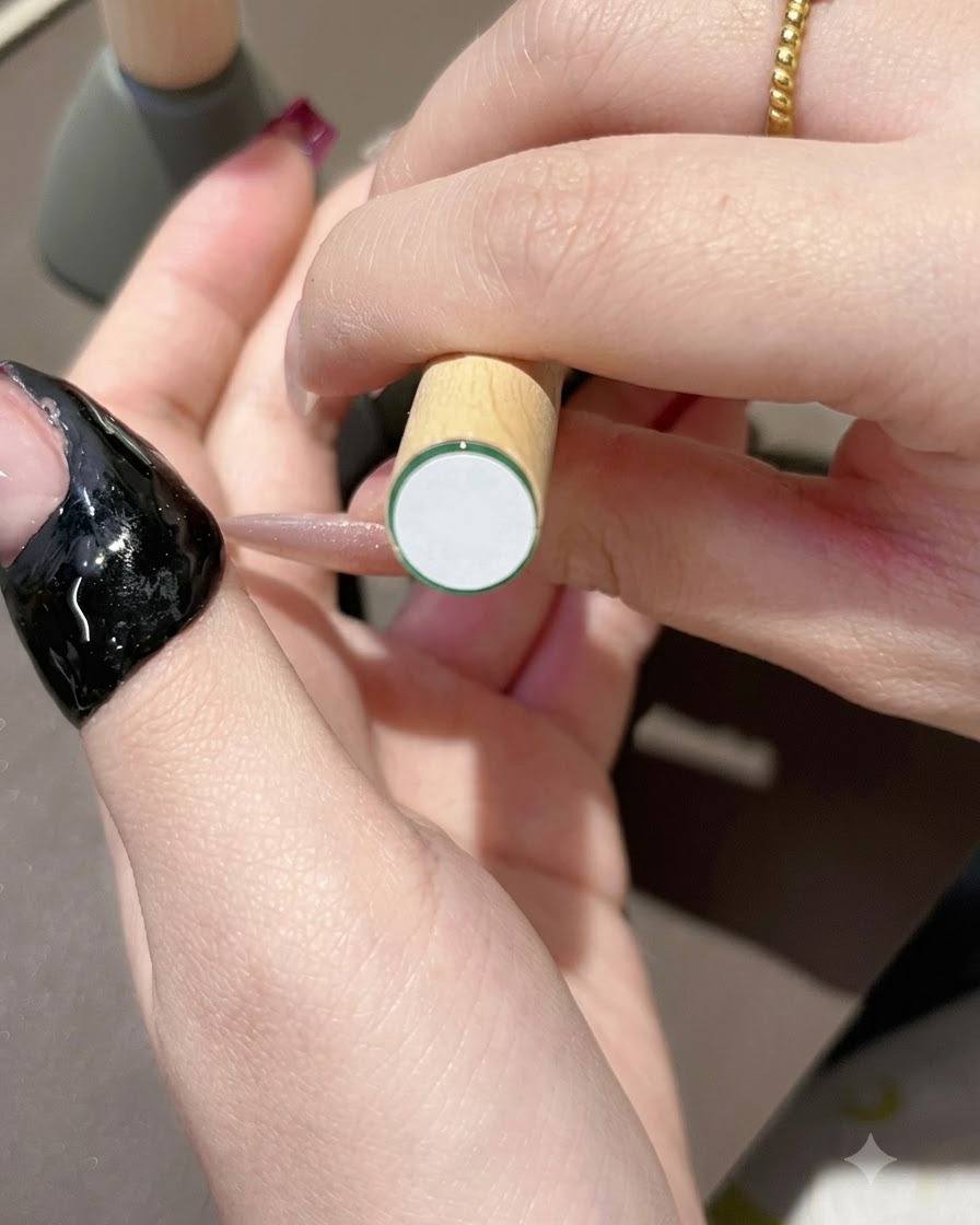 Ein Pinsel trägt dunkelvioletten Gelack auf die Spitze eines naturnah aussehenden Nagels auf.