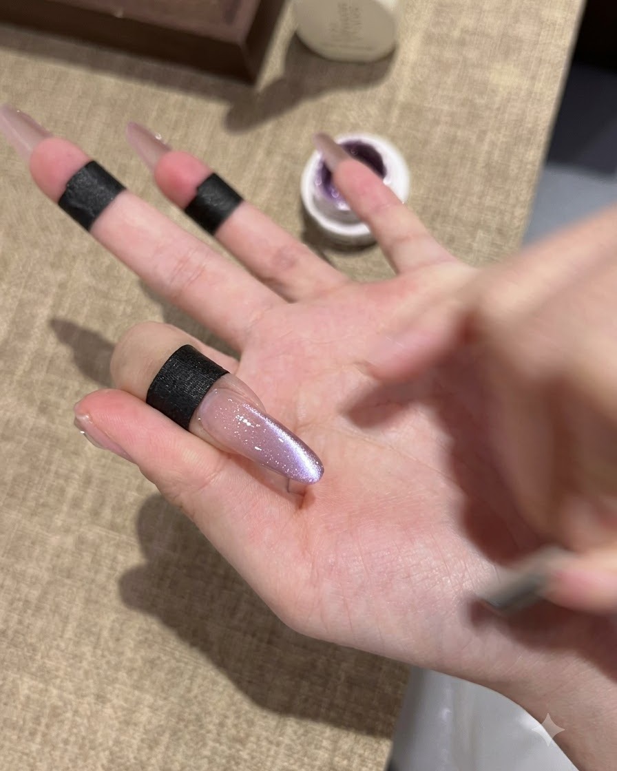 Nahaufnahme eines länglichen Mandel-Nagels mit frisch fixiertem violetten Cat-Eye-Gel-Lack und schimmerndem Reflexionszentrum.