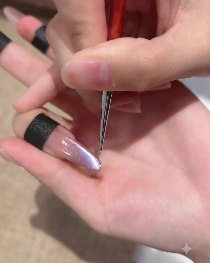Ein feiner Liner-Pinsel zieht eine sehr dünne Linie aus glitzerndem Silbergel entlang der Seitenlinie eines violetten Cat-Eye-Nagels.