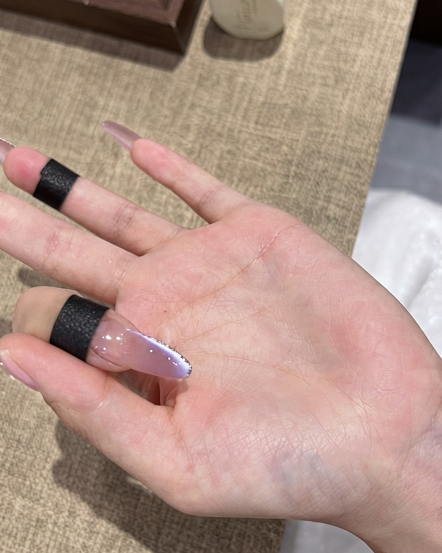 Ein Pinsel trägt einen finalen Hochglanz-Top Coat auf einen violetten Ombré-Cat-Eye-Nagel mit feinem Silberglitter-Rand auf.