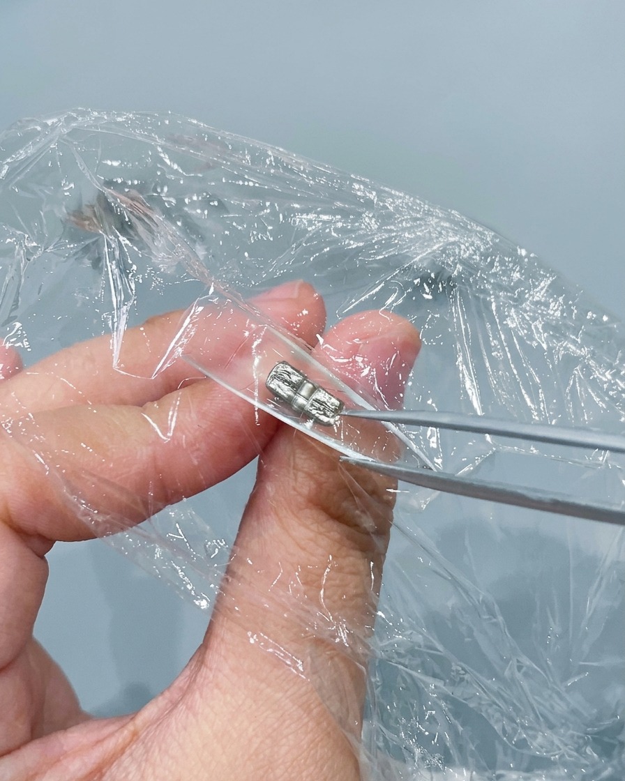 Eine Metallpinzette kneift und knittert Frischhaltefolie, die in eine klare Nagelspitze gedrückt wurde.