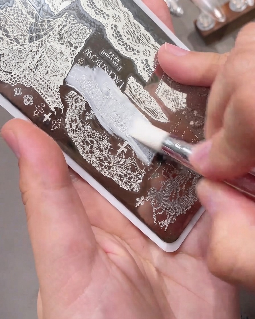 Eine Abstreifkarte gleitet glatt über eine gravierte Metall-Nagel-Stamping-Platte, die mit weißem Gel-Polish gefüllt ist.