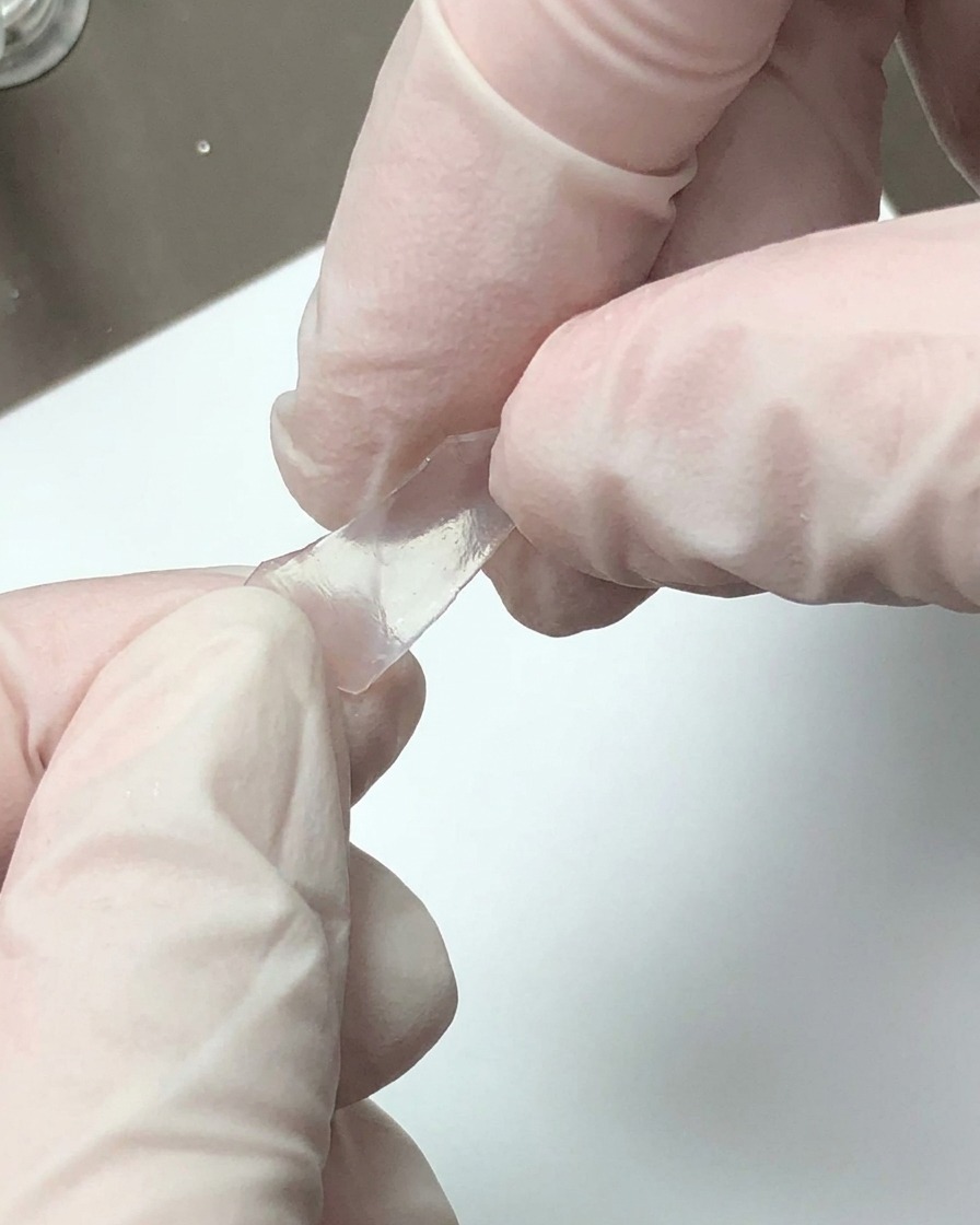 Mit Handschuhen bekleidete Hände brechen eine transparente dekorative Platte in kleine Fragmente.