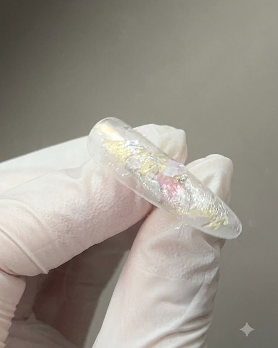 Ein Magnetwerkzeug wird dicht über einen glänzenden, mit Gel beschichteten Nagel gehalten, um die reflektierenden Cat-Eye-Magnetpartikel zu formen.
