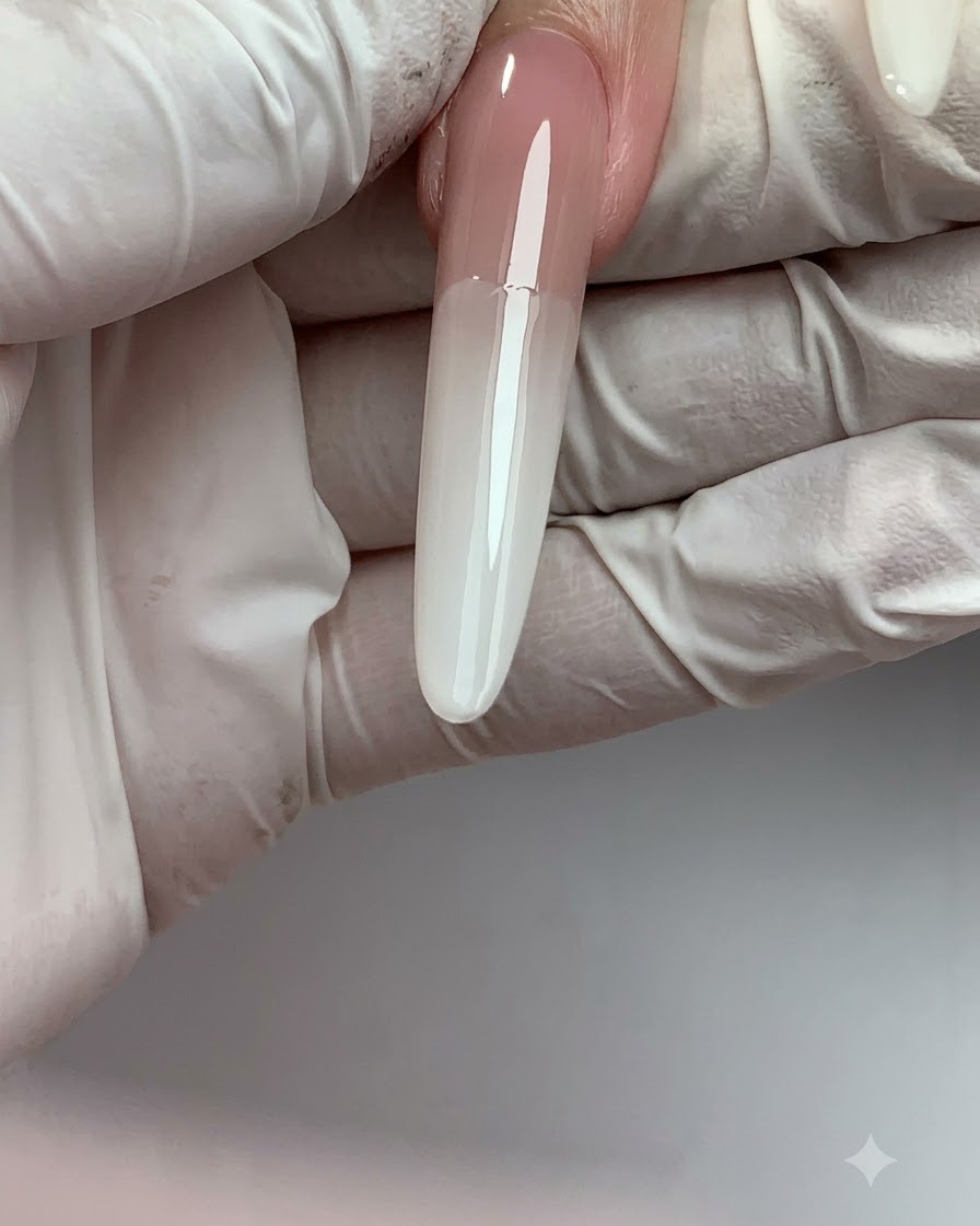 Ein langer Verlängerungsnagel zeigt einen glatten Ombré-Farbverlauf von Nude oben bis Milchweiß an der Spitze.