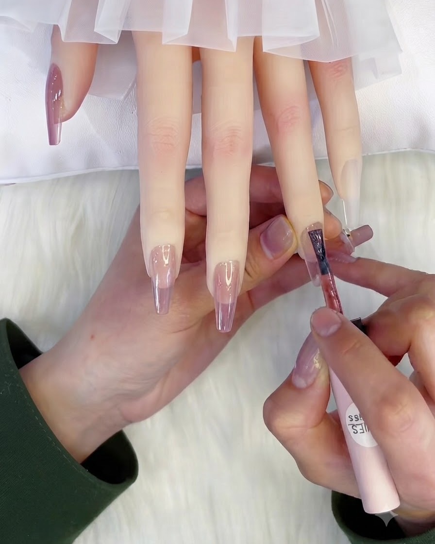 Ein Pinsel trägt eine zweite Schicht durchscheinendes rosa Gel auf einen Nagel auf.