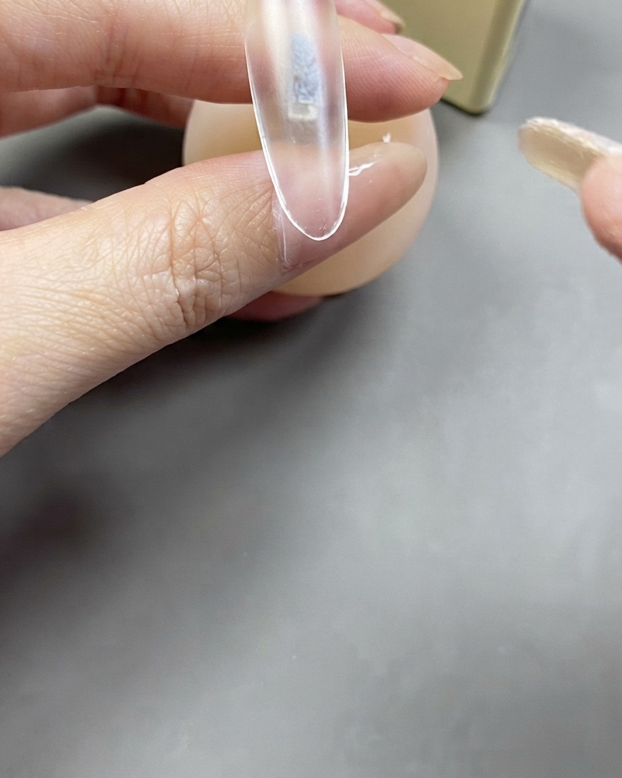 Ein Pinsel trägt eine klare Schicht Base Gel auf eine klare Nagelverlängerung auf.