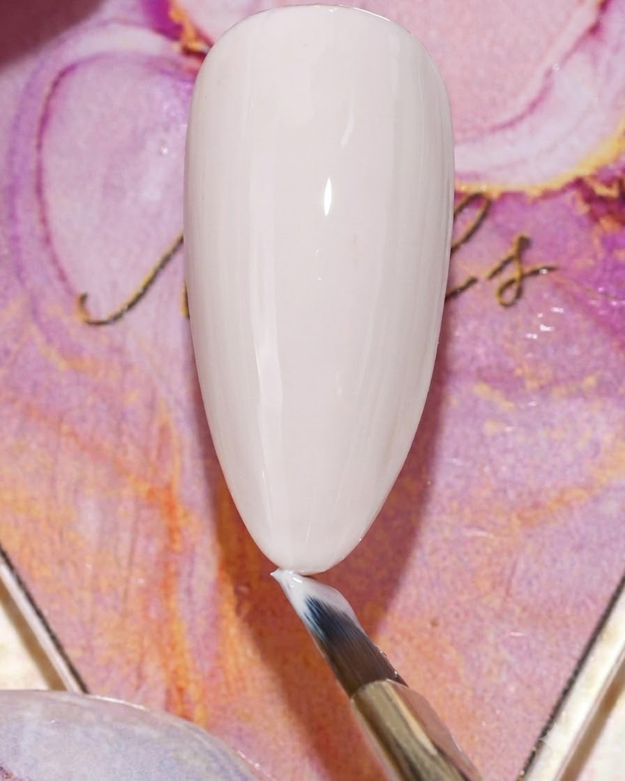 Ein Pinsel trägt einen matten Top-Coat über die beige Gel-Basis einer Nagelspitze auf.